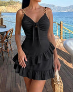 Mireia | Vestido corto de tirantes con cadena, lazo frontal, volantes en el bajo y espalda descubierta.